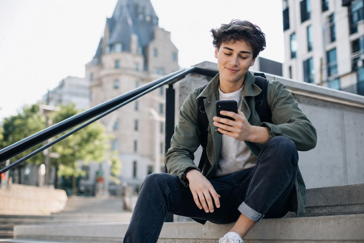 Un jeune homme décontracté assis sur des marches en ville, qui jette un coup d'oeil à son téléphone, détendu et accessible.